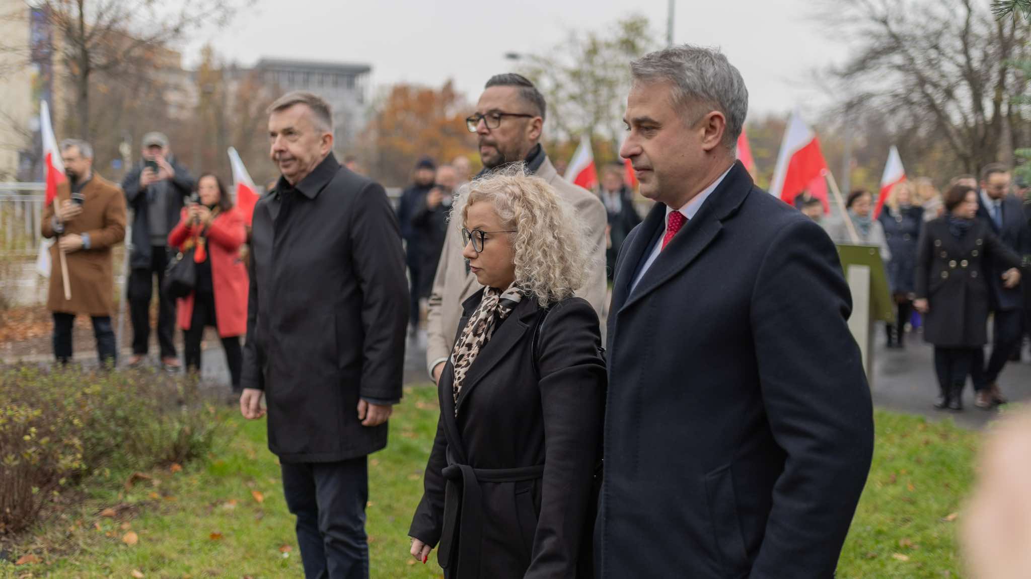 Grupa uczestników z flagami spaceruje podczas obchodów 106. rocznicy powołania rządu Ignacego Daszyńskiego.