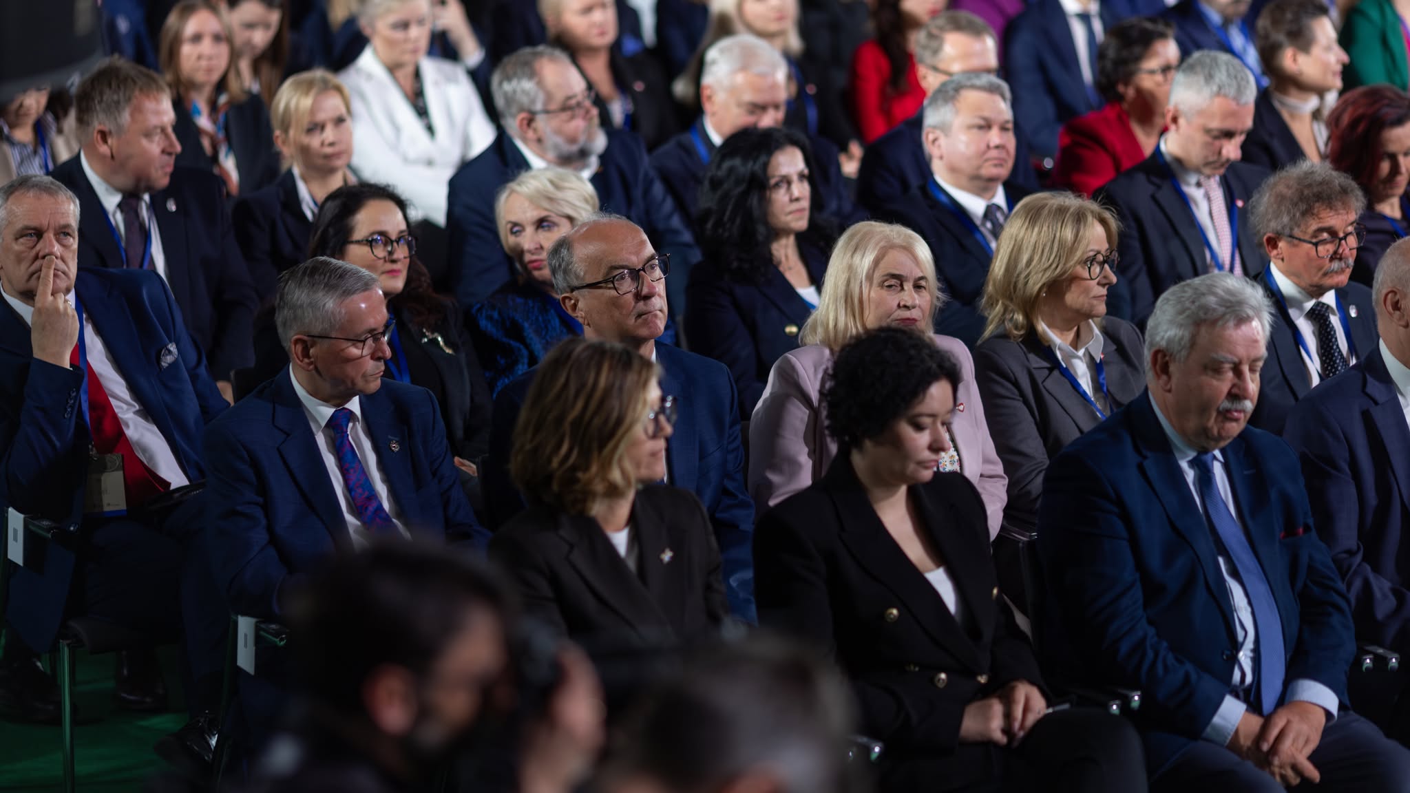 Grupa osób ubranych formalnie siedzi na widowni podczas uroczystości upamiętniającej 1000. rocznicę koronacji Bolesława Chrobrego.