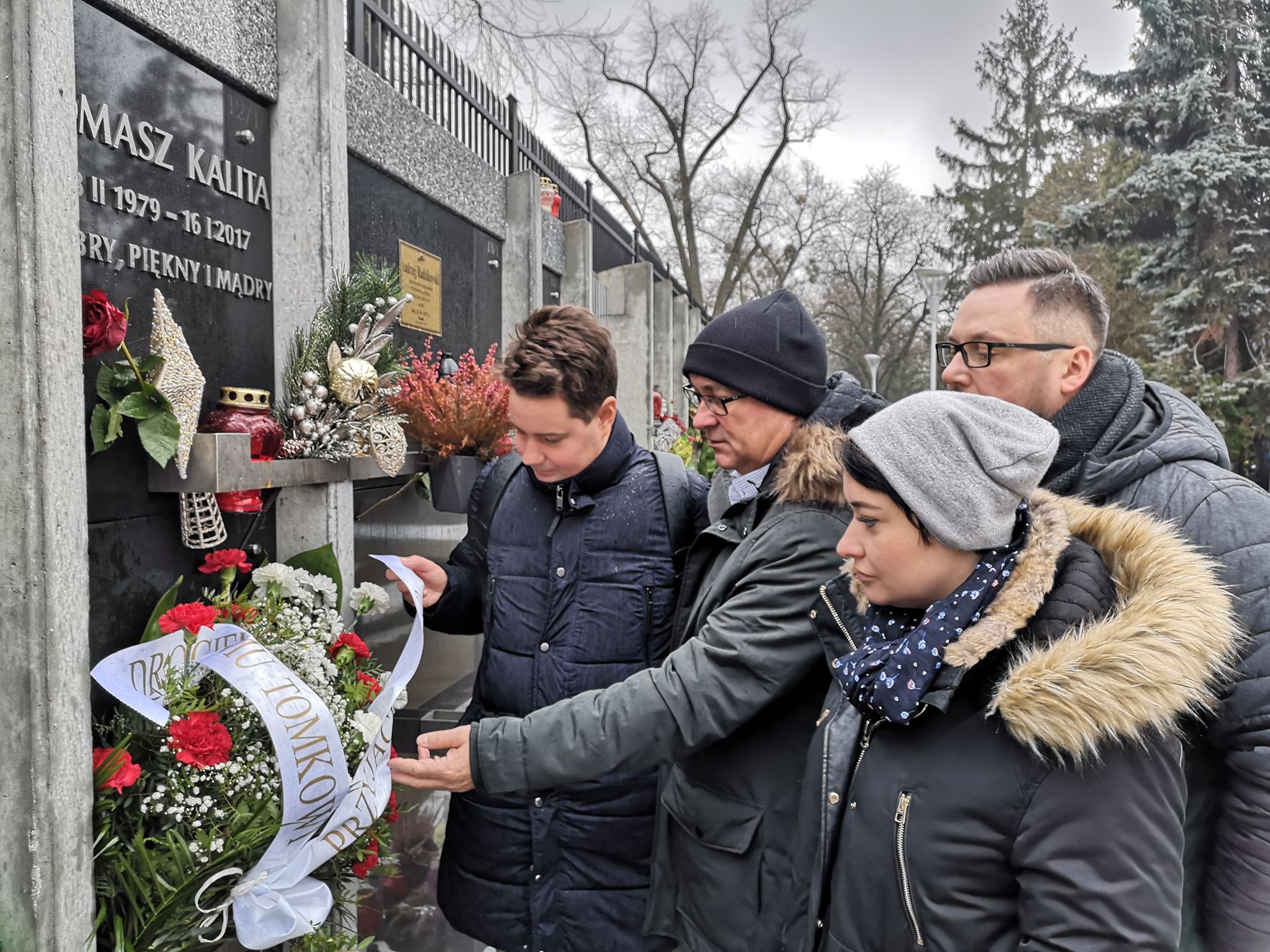 Grupa ludzi składa kwiaty przed tablicą upamiętniającą Tomasza Kality.