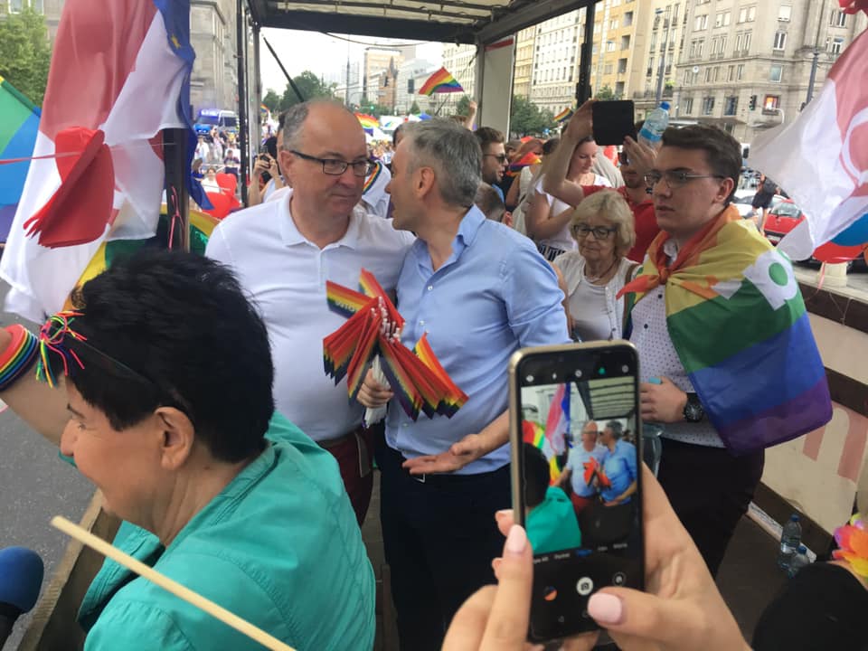 Uczestnicy Parady Równości 2019 stoją na platformie, trzymają tęczowe flagi i robią zdjęcia w tłumie na ulicy.
