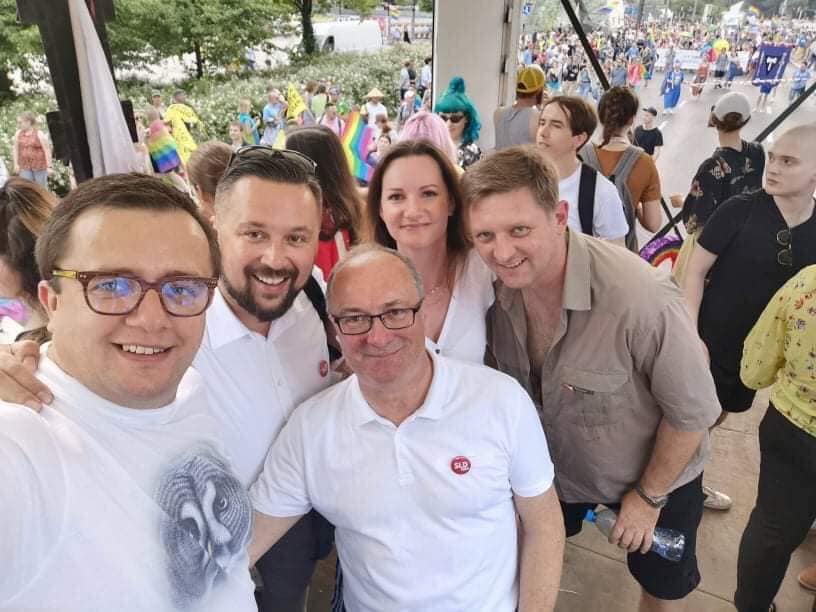 Grupa pięciu osób robiących wspólne selfie podczas Parady Równości 2019, w tłumie uczestników i tęczowych flag w tle.