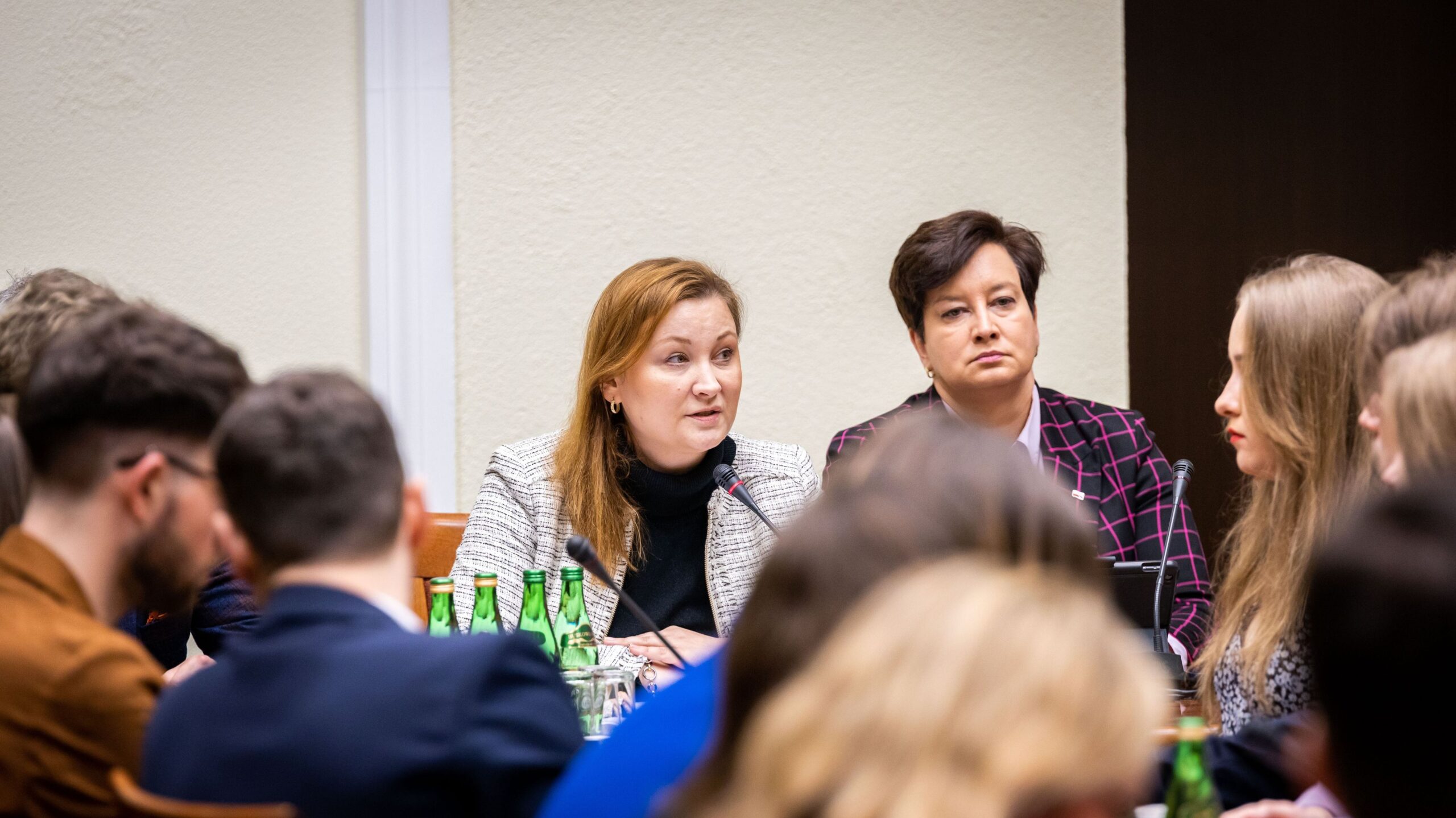Uczestnicy okrągłego stołu omawiają problemy w psychiatrii dziecięcej podczas konferencji; w centrum kadru dwie kobiety mówią do mikrofonów.