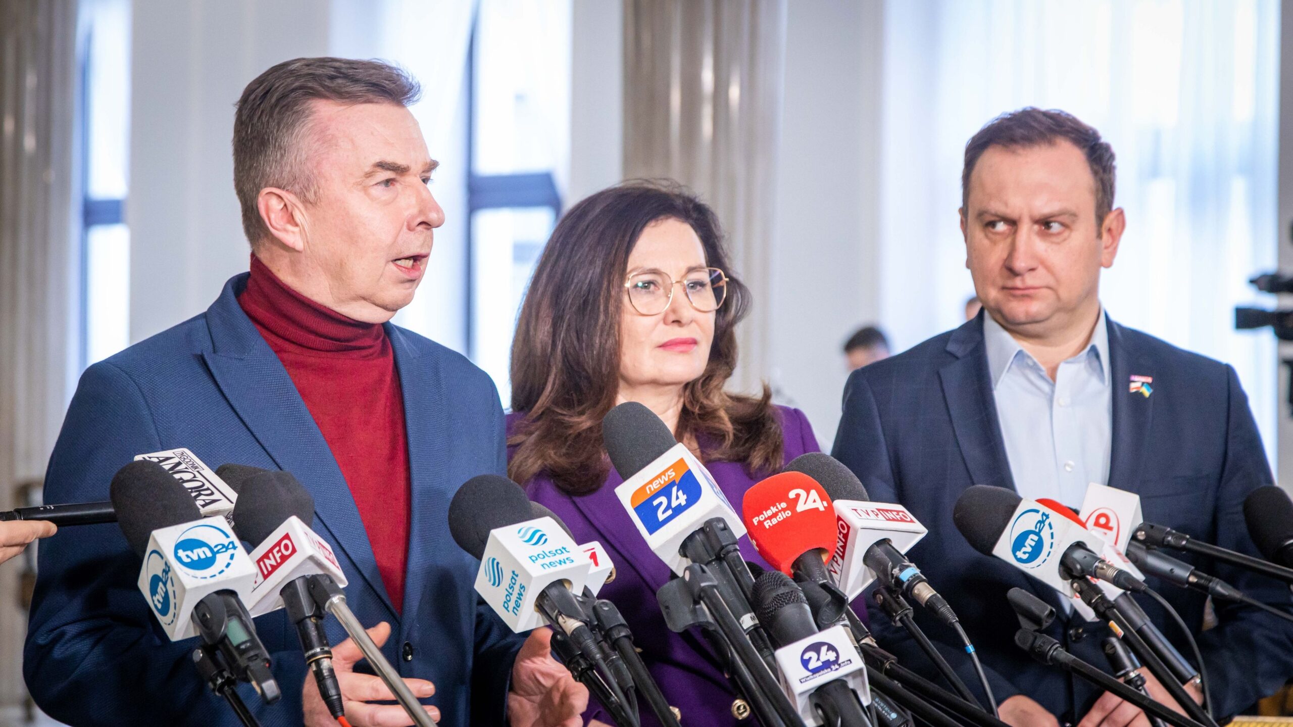 Trzy osoby w garniturach stoją przed licznymi mikrofonami podczas konferencji prasowej dotyczącej sporu między NIK a Orlen.