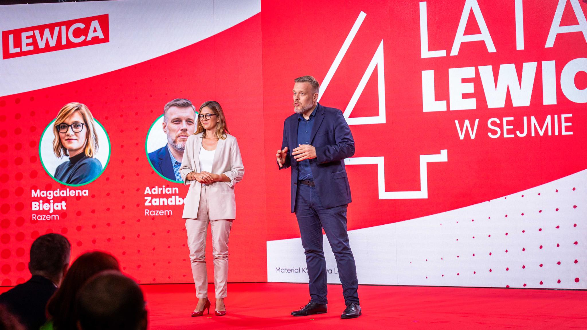 Scena konferencji Lewicy: dwie osoby w formalnych strojach przemawiają na czerwonym tle z dużym banerem Lewicy i napisem „4 lata Lewicy w Sejmie”, obok widoczne okrągłe portrety polityków.