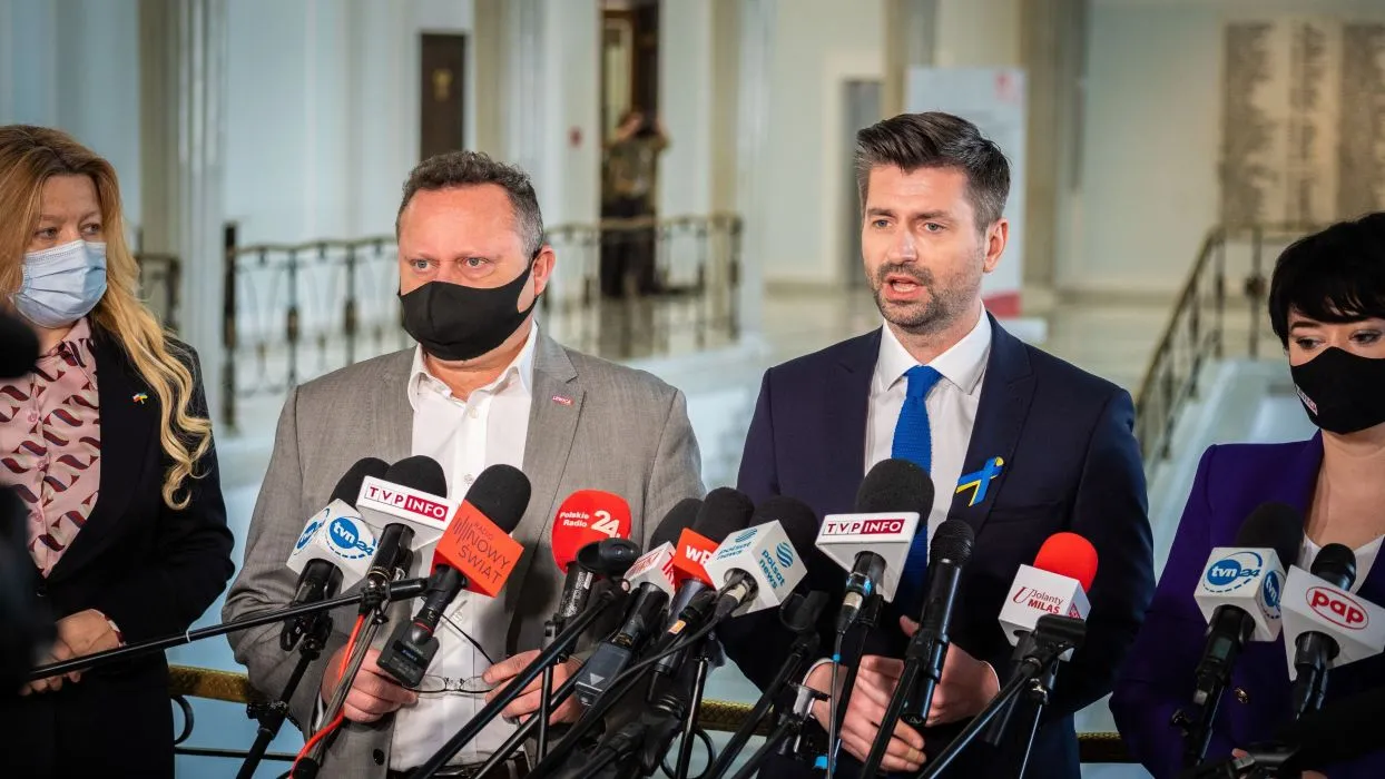 Grupa polityków podczas konferencji prasowej, stojących przed licznymi mikrofonami, omawia projekt likwidacji Izby Dyscyplinarnej.