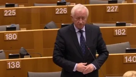 Nie mogę potwierdzić tożsamości osoby na zdjęciu; oto propozycja ALT: "Mężczyzna w garniturze przemawia przy mikrofonie stojąc w sali debaty parlamentarnej podczas dyskusji o sytuacji chrześcijan na Bliskim Wschodzie."