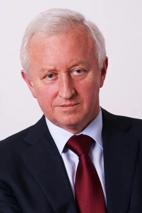 Portret starszego mężczyzny w granatowym garniturze i bordowym krawacie na jasnym tle.