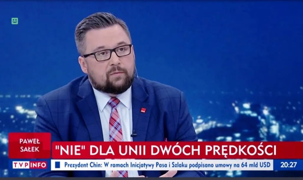 Mężczyzna w garniturze i okularach siedzi w studiu telewizyjnym; na dole ekranu widnieje czerwony pasek z napisem 'NIE DLA UNII DWÓCH PRĘDKOŚCI' oraz logo TVP INFO.
