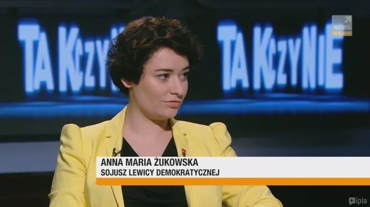 Kobieta w żółtej marynarce udziela wywiadu w studiu telewizyjnym, a u dołu ekranu widoczny jest podpis z jej imieniem i przynależnością polityczną.