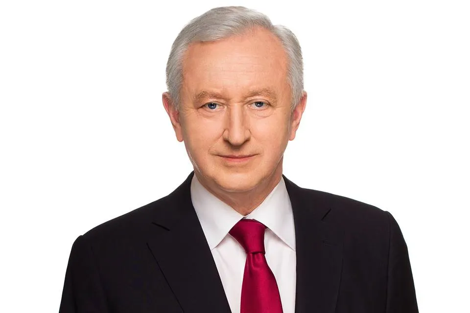 Portret starszego mężczyzny w czarnym garniturze, białej koszuli i czerwonym krawacie na białym tle.