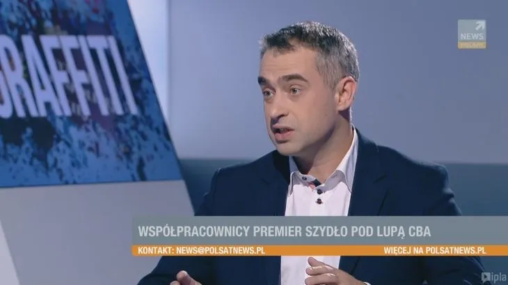 Mężczyzna w marynarce gestykuluje podczas wywiadu w studiu telewizyjnym, a na pasku informacyjnym widnieje napis "Współpracownicy premier Szydło pod lupą CBA".