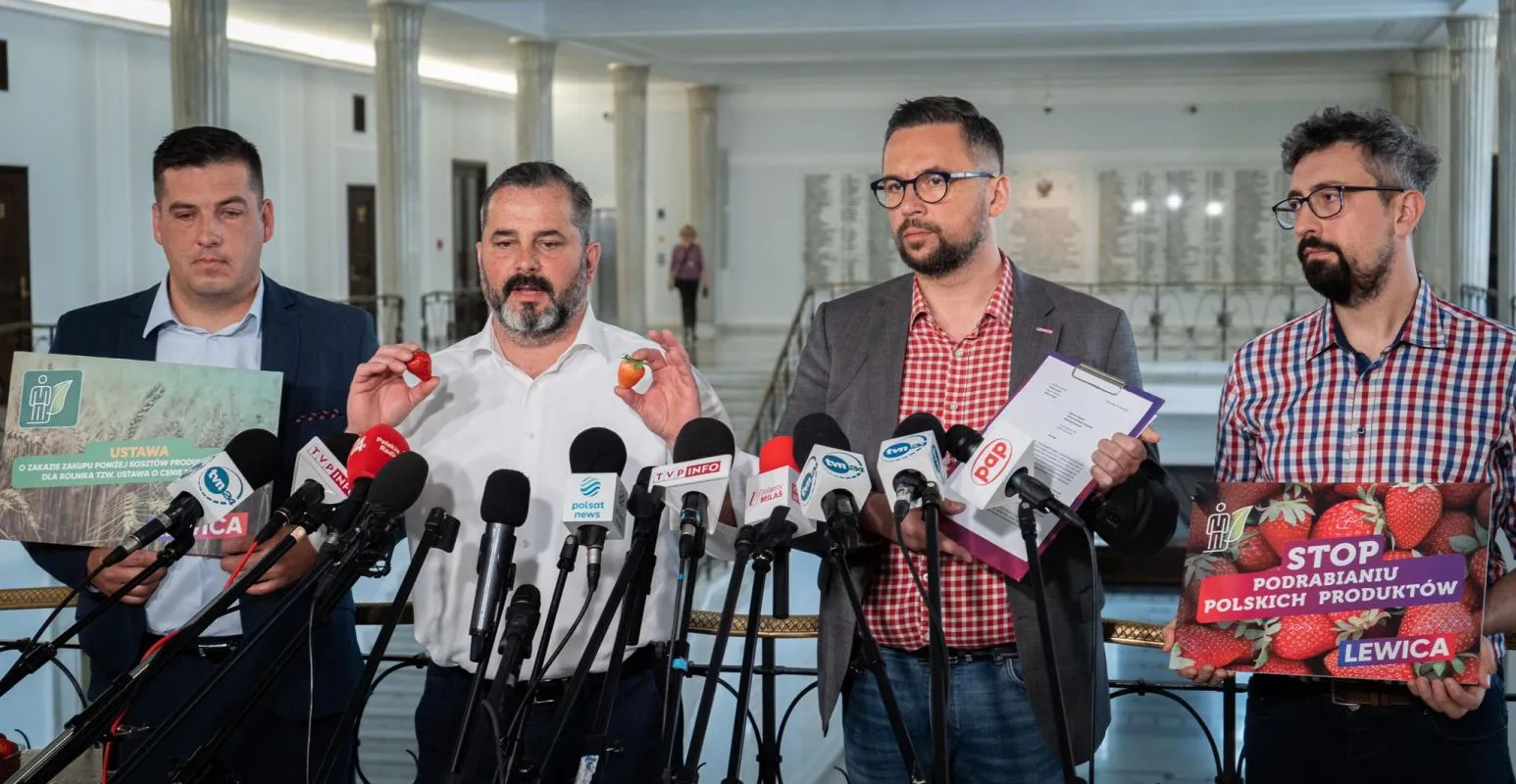 Czterech mężczyzn na konferencji prasowej Lewicy, trzymają plakaty dotyczące polskich truskawek i podrabiania produktów, stojąc za licznymi mikrofonami.