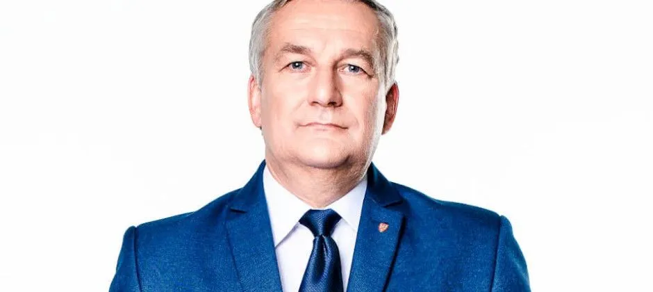 Portret mężczyzny w granatowym garniturze i niebieskim krawacie na białym tle.