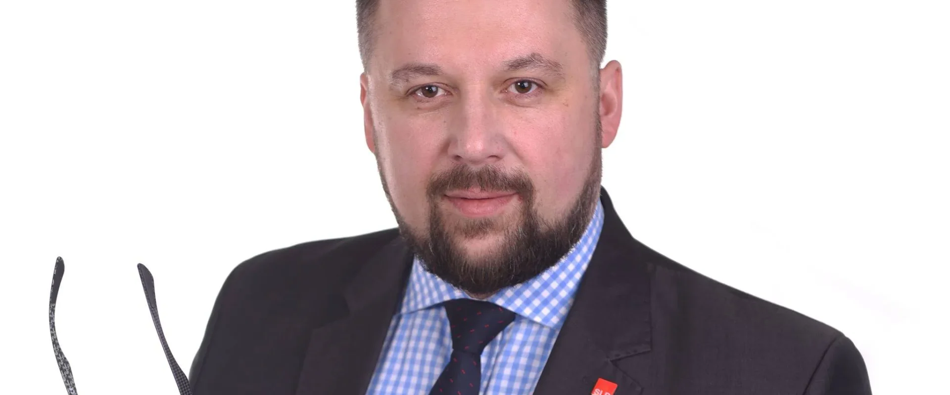 Portret mężczyzny w garniturze, trzymającego okulary w lewej ręce, na białym tle.