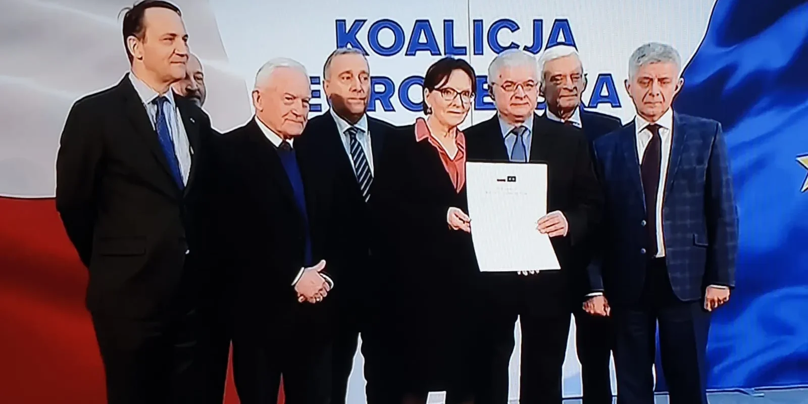 Grupa premierów i ministrów spraw zagranicznych podczas wspólnej konferencji nawołująca do szerokiego porozumienia na wybory europejskie, trzymająca podpisany dokument, na tle flag Polski i Unii Europejskiej oraz banera z napisem KOALICJA EUROPEJSKA.