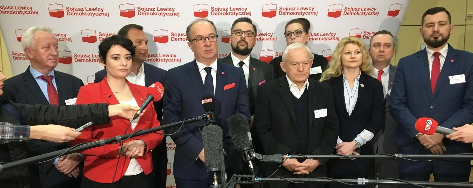 Grupa polityków stojących na konferencji prasowej przed ścianką z logotypem Sojuszu Lewicy Demokratycznej.