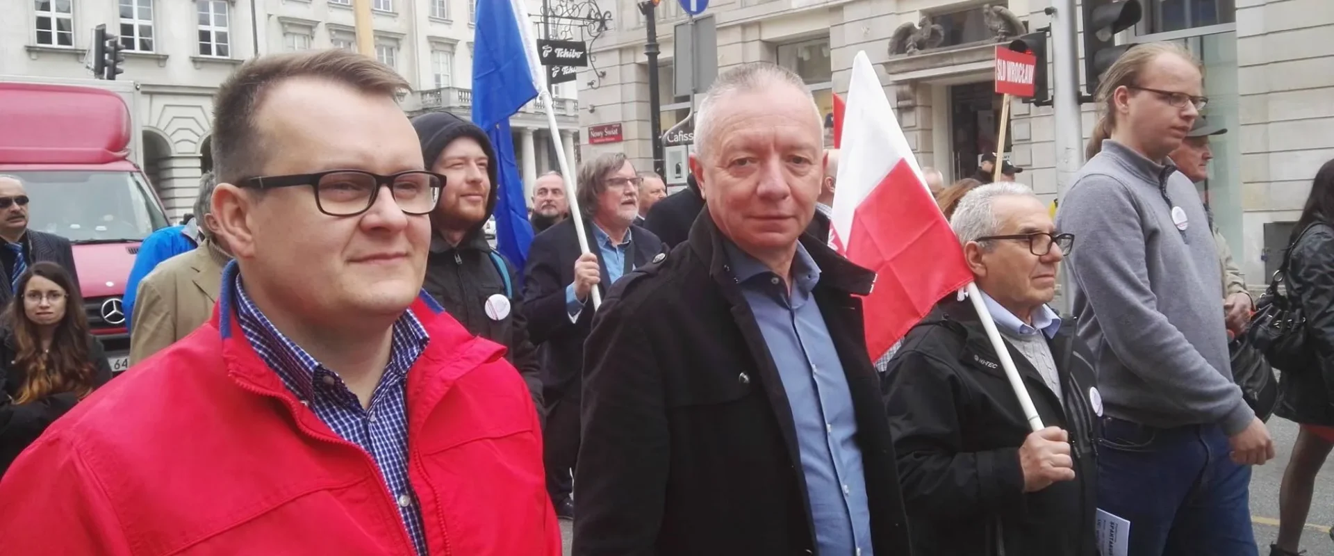 Grupa ludzi idzie ulicą podczas demonstracji, trzymając baner „SLD WROCŁAW” oraz flagi Polski.