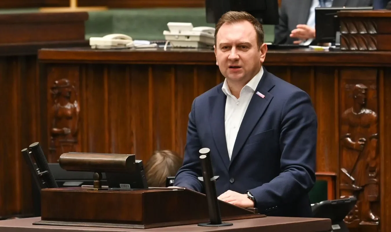 Polityk w garniturze przemawia z mównicy w sali obrad.