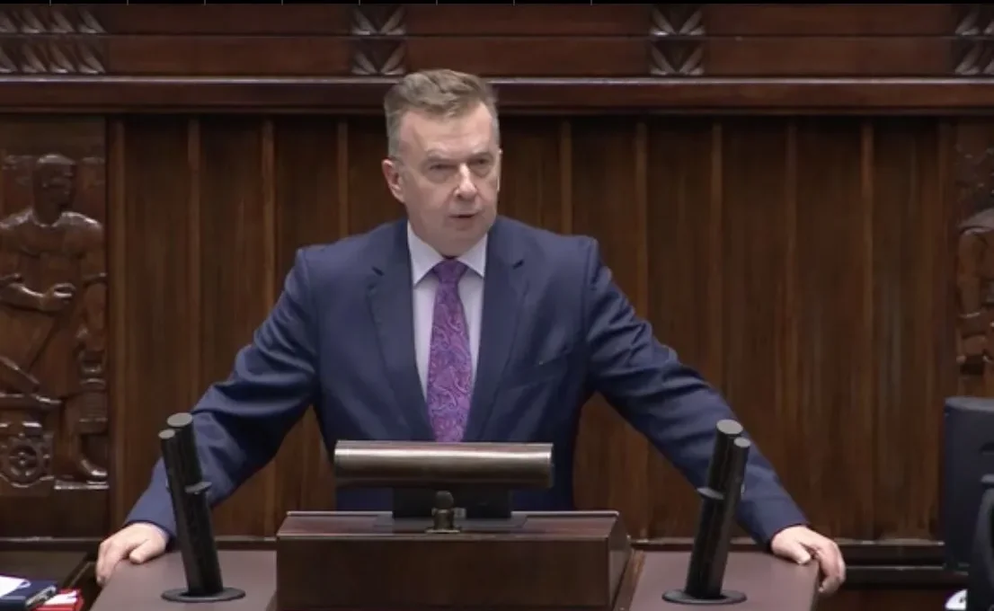 Mężczyzna w garniturze przemawia z mównicy w sali obrad, zapowiadając restrykcyjne zmiany w systemie wizowym.