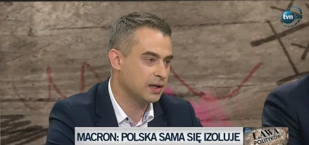 Mężczyzna w marynarce wypowiada się w studio telewizyjnym, na dole pasek z napisem "MACRON: POLSKA SAMA SIĘ IZOLUJE".