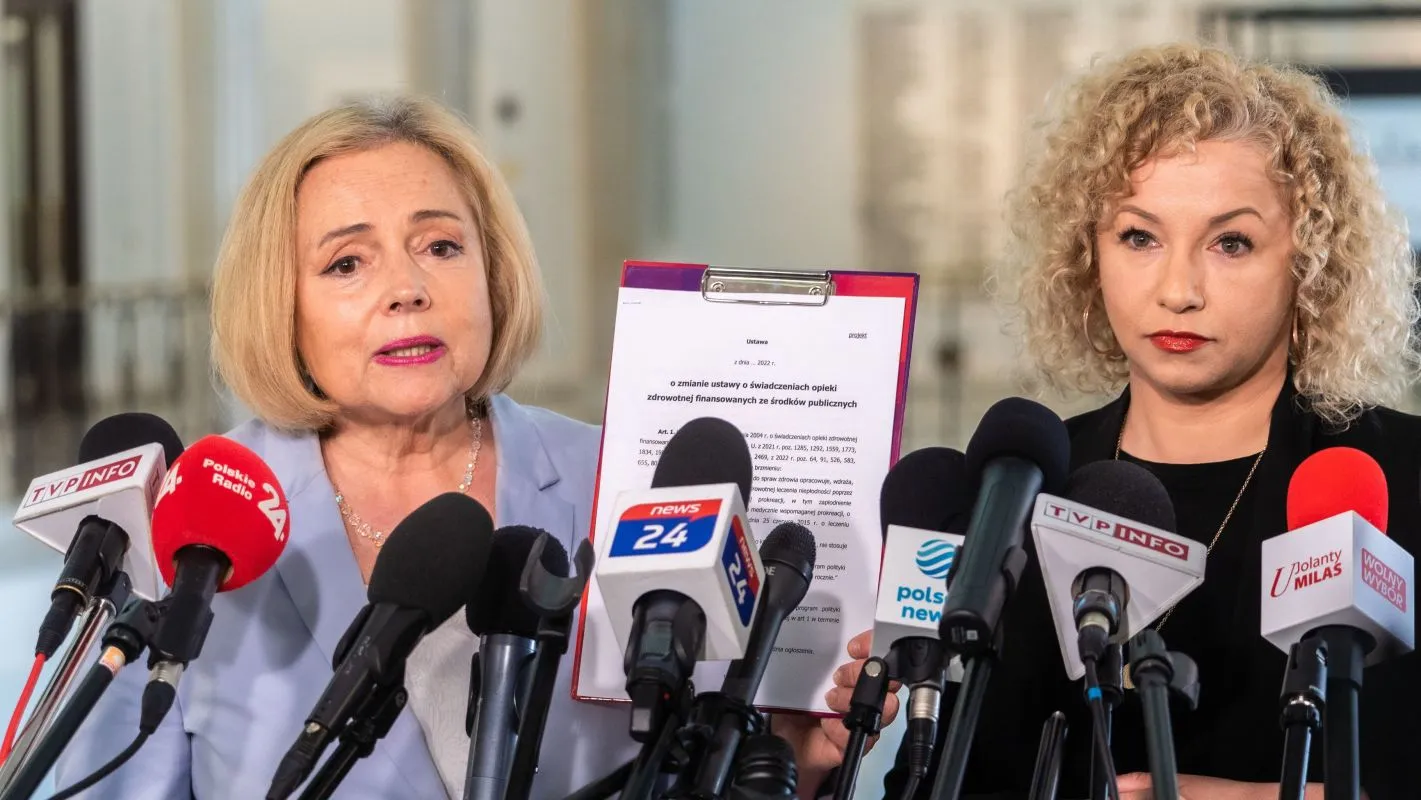 Konferencja prasowa, na której jedna z mówczyń prezentuje dokument dotyczący zmian w ustawie o świadczeniach opieki zdrowotnej.