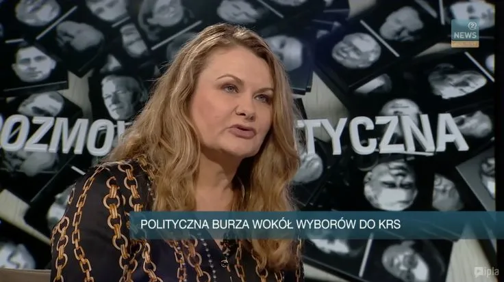 Kobieta mówi w studiu telewizyjnym, na dole ekranu pasek z napisem „POLITYCZNA BURZA WOKÓŁ WYBORÓW DO KRS”, a w tle czarno-biały kolaż twarzy.