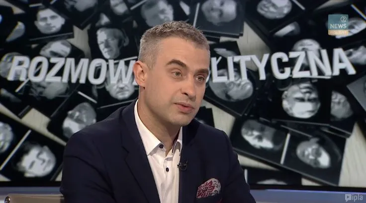 Mężczyzna w garniturze rozmawia w studiu telewizyjnym, a w tle widoczny jest napis „ROZMOWA POLITYCZNA” i kolaż fotografii.
