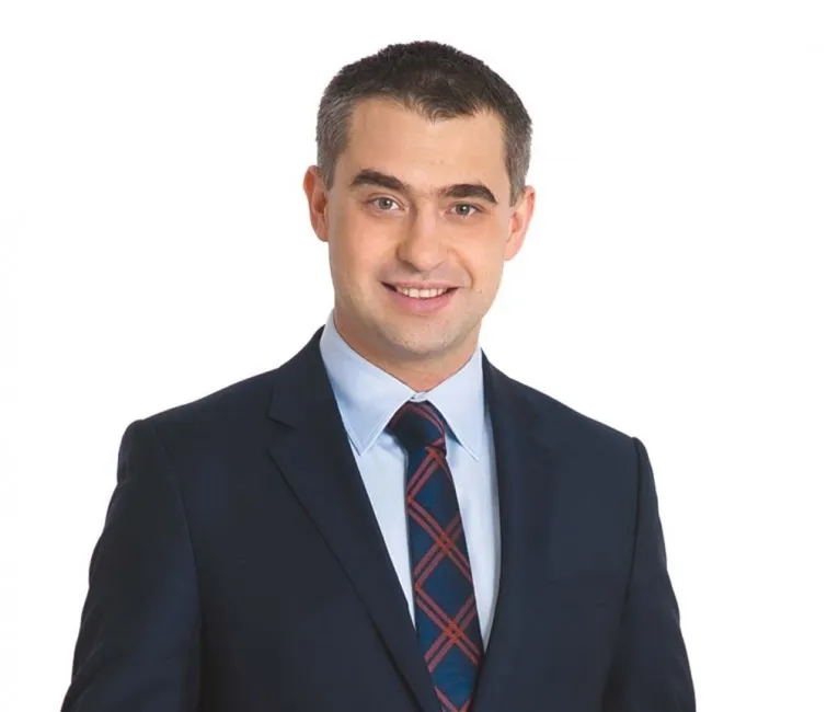 Portret mężczyzny w granatowym garniturze i kraciastej krawacie, ilustracja do wypowiedzi o Forum Ekonomicznym w Krynicy.