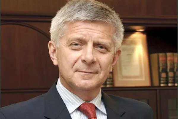 Portret mężczyzny w garniturze z czerwonym krawatem w biurze, na tle książek, przygotowującego się do poważnej rozmowy o podatku od transakcji finansowych i podatku cyfrowego.