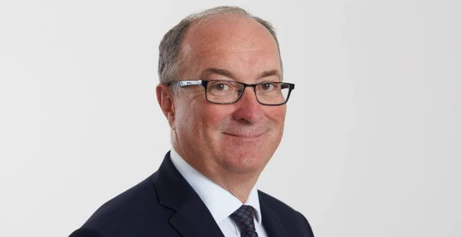 Portret mężczyzny w garniturze i okularach, uśmiechnięty, na białym tle.