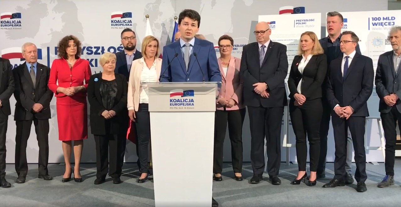 Grupa polityków stoi na scenie podczas konferencji prasowej Koalicji Europejskiej, przy centralnym pulpicie z logiem Koalicji Europejskiej.
