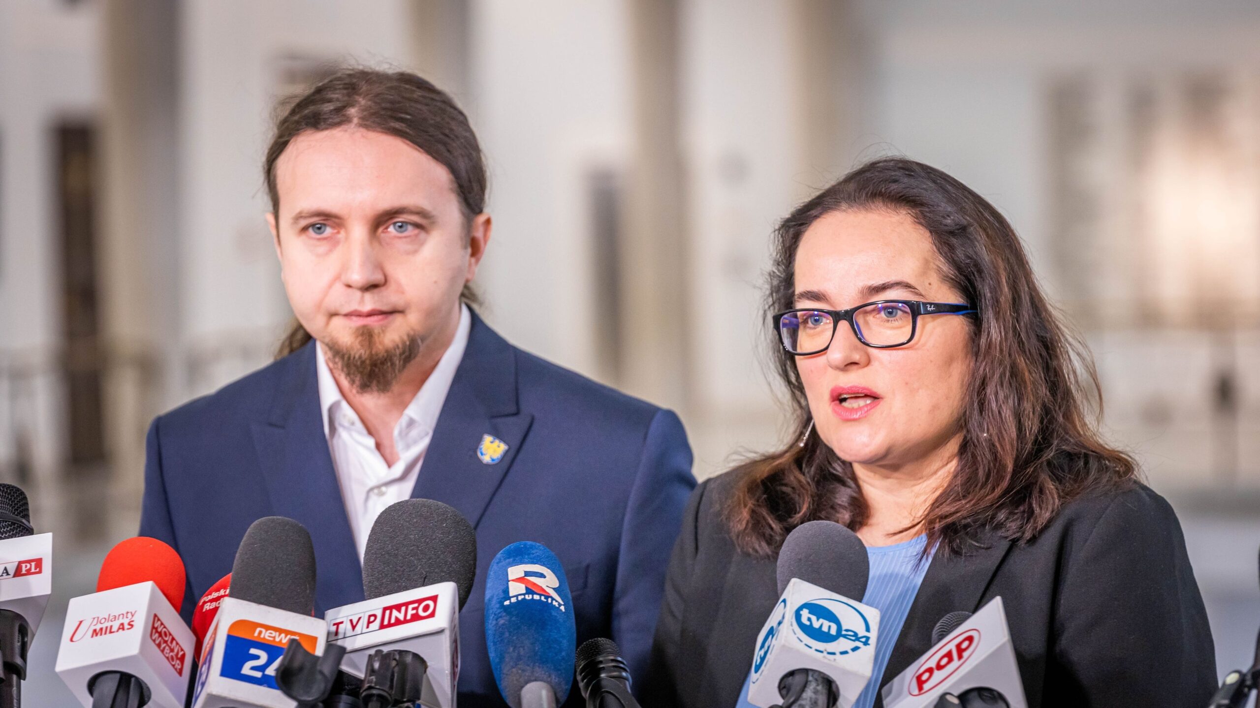 Para polityków przemawia na konferencji prasowej dotyczącej Konwencji Stambulskiej w Unii Europejskiej, stojąc przed licznymi mikrofonami.