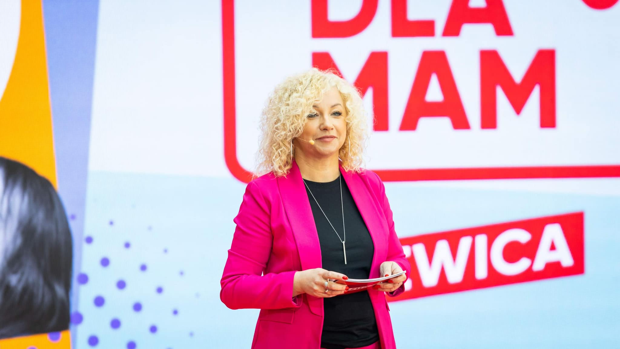 Prelegentka stojąca na scenie podczas Konwencji Mamy plan dla mam, ubrana w różowy żakiet i trzymająca kartki.