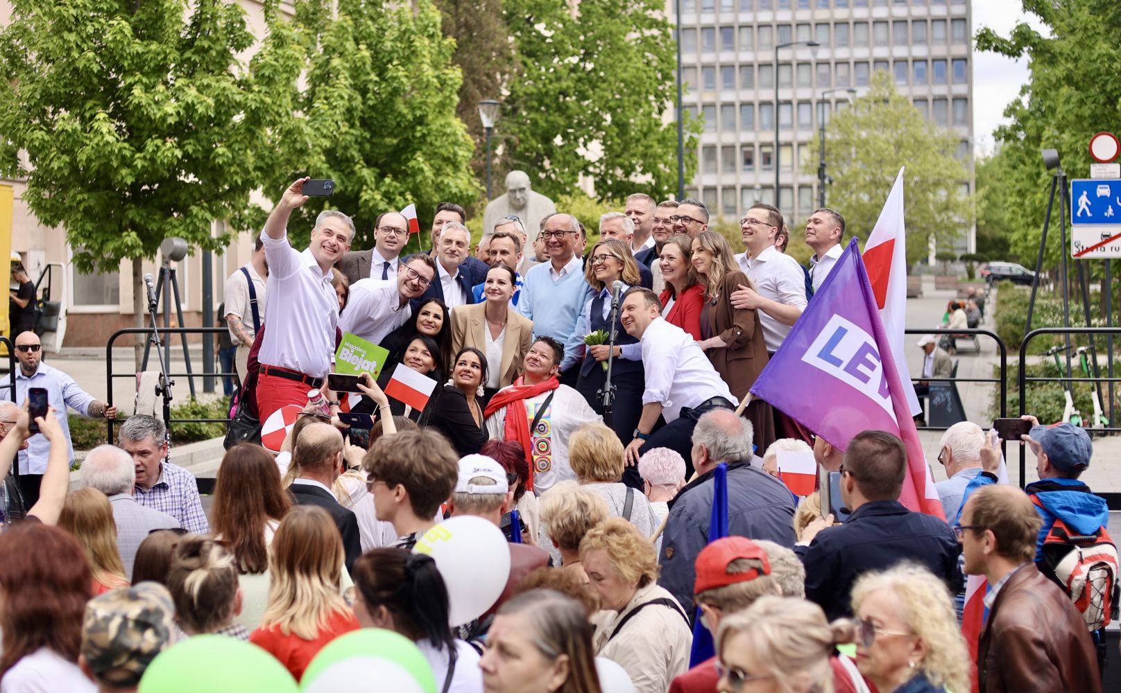 Duża grupa ludzi na podium podczas Święta Pracy 2025, robią wspólne selfie, wśród tłumu widoczne polskie flagi.