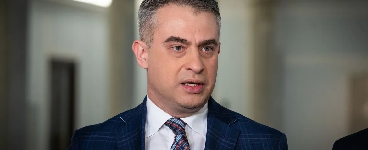 Mężczyzna w granatowym garniturze w kratę i białej koszuli z krawatem rozmawia podczas wywiadu w biurze.