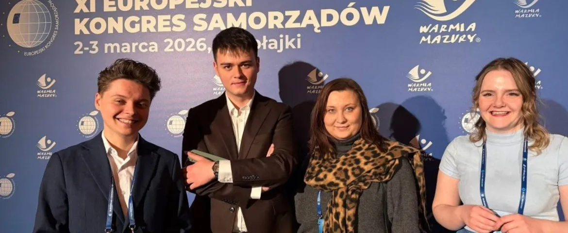 Czterech młodych ludzi stoi przed niebieskim tłem z napisem XI Europejski Kongres Samorządów, 2–3 marca 2026, Warmia Mazury; wszyscy uśmiechnięci i mają identyfikatory na smyczkach.