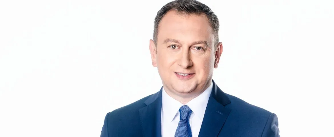 Portret mężczyzny w granatowym garniturze i niebieskim krawacie na białym tle.