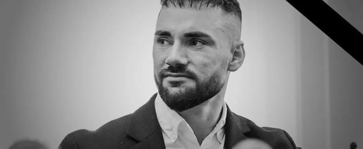 Czarnobiały portret mężczyzny w garniturze i białej koszuli, patrzącego w lewo, z krótkimi włosami i brodą; w prawym górnym rogu widoczna czarna wstążka żałobna.
