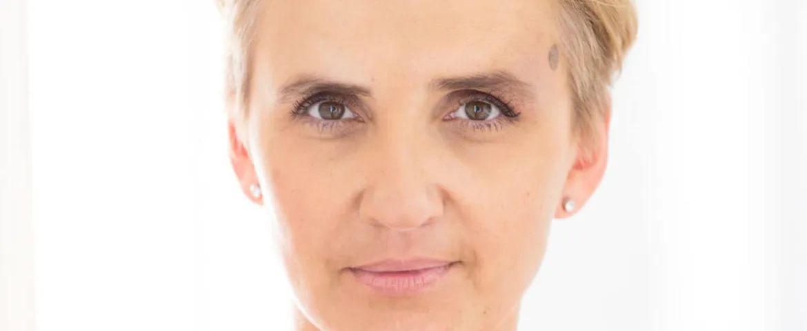 Kobieta o krótkich blond włosach patrzy prosto w kamerę na jasnym, białym tle.