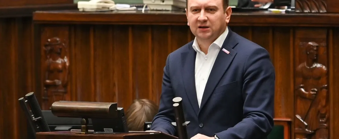 Mężczyzna w granatowym garniturze przemawia podczas posiedzenia w sali obrad.