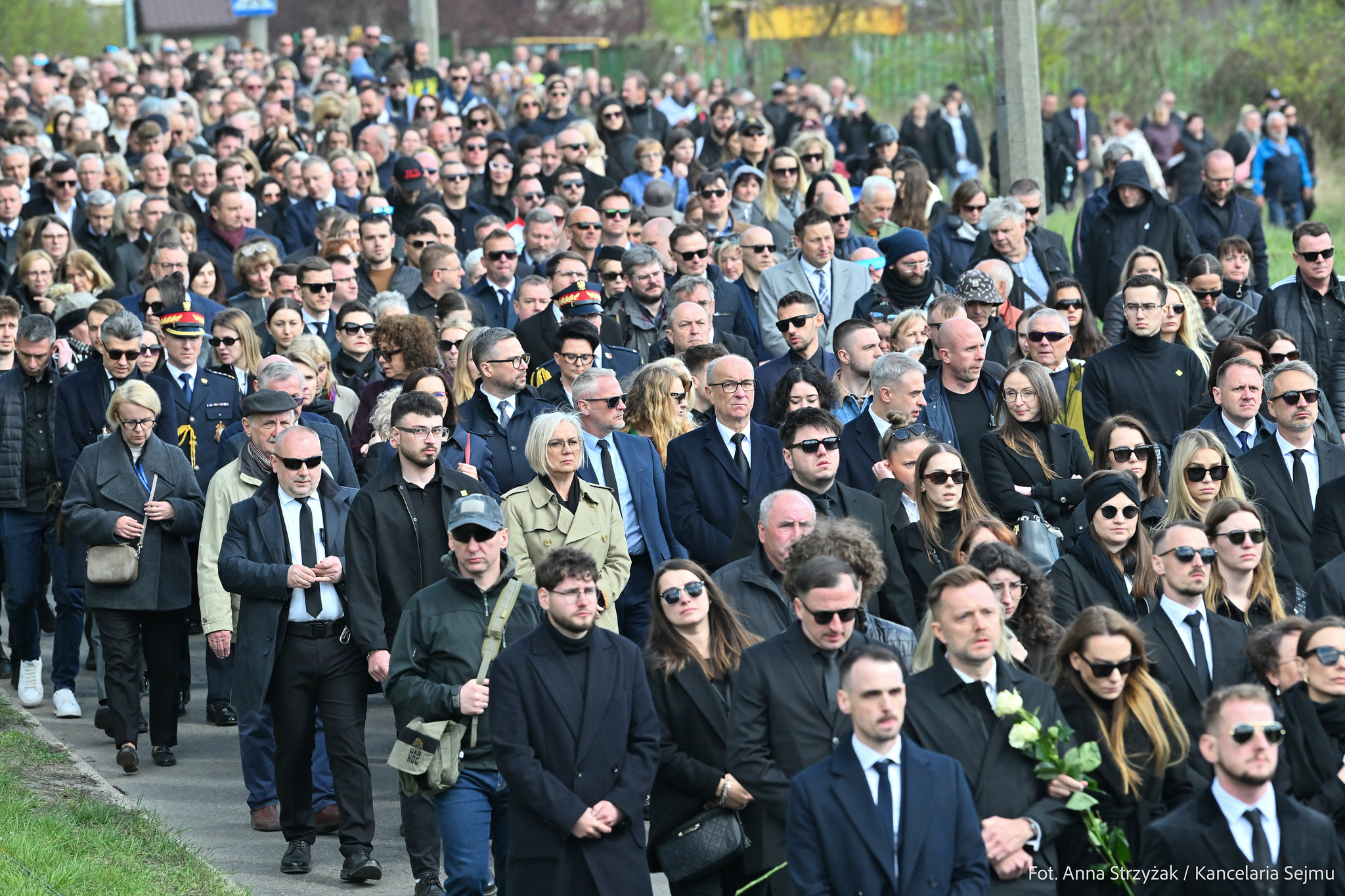 Ogromny tłum ludzi w czarnych ubraniach maszeruje ulicą podczas żałobnej procesji.